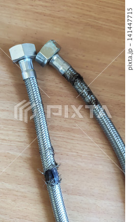 Damaged flexible hose with a metal braided sheath showing visible tears, corrosion, and signs of wear. Damaged flexible hose with a metal braided sheath showing visible tears, corrosion, and signs of wear. 141447715
