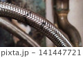 Close up of a worn braided water hose with rust and damaged protective metal mesh. 141447721