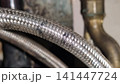 Flexible metal braided hose displaying corrosion, torn outer braid, and long-term material deterioration. 141447724