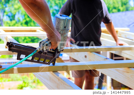 Construction workers use air nail gun to secure wooden beams in an outdoor setting 141447995