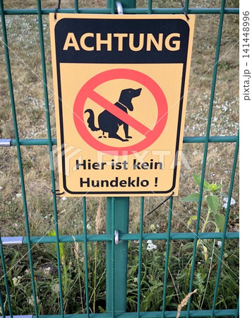 A warning sign in German on a green fence, prohibiting dog walking and allowing dogs to relieve themselves. 141448996