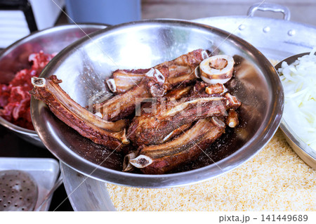 Bowl contains pieces of meat with bones, alongside rice other ingredients on countertop in kitchen. 141449689