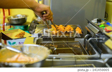 Chef preparing crispy fried chicken in a commercial kitchen with a deep fryer 141450005
