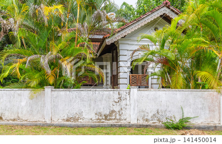 Traditional tropical colonial house surrounded by lush garden vegetation and white boundary wall Traditional tropical colonial house surrounded by lush garden vegetation and white boundary wall 141450014