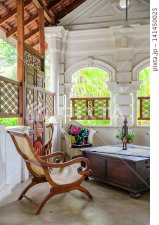 Elegant colonial villa lounge with wooden armchair, wicker seating and tropical garden views Elegant colonial villa lounge with wooden armchair, wicker seating and tropical garden views 141450025