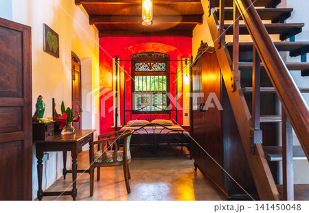 Stylish colonial bedroom with wooden staircase, vintage furniture and vibrant red accent wall Stylish colonial bedroom with wooden staircase, vintage furniture and vibrant red accent wall 141450048