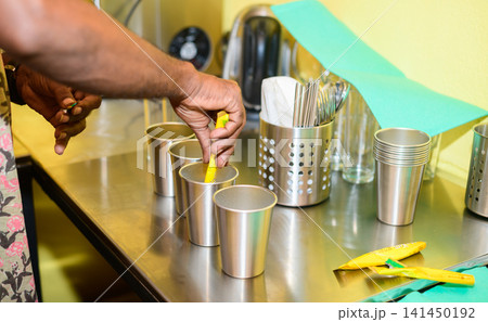 Bartender preparing instant beverage sachets in stainless steel cups on a commercial kitchen counter Bartender preparing instant beverage sachets in stainless steel cups on a commercial kitchen counter 141450192