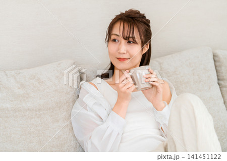 部屋でコーヒーを飲みながらリラックスしてくつろぐアジア人女性 141451122