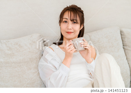 部屋でコーヒーを飲みながらリラックスしてくつろぐアジア人女性 部屋でコーヒーを飲みながらリラックスしてくつろぐアジア人女性 141451123