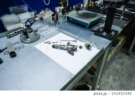 Disassembled diesel fuel injector with components placed on white paper sheet on mechanic workbench in auto repair workshop Disassembled diesel fuel injector with components placed on white paper sheet on mechanic workbench in auto repair workshop 141452340
