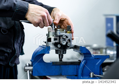 Mechanic hands repairing high pressure fuel pump in vice tool close up diesel fuel injection system tnhv maintenance 141452341