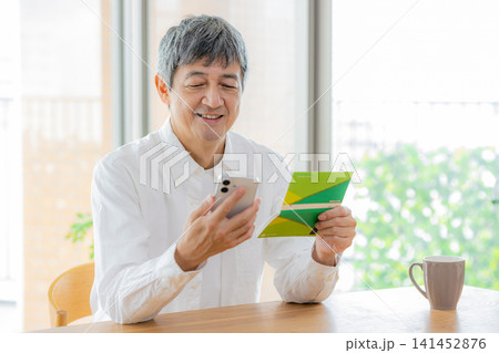 通帳とスマホを持つシニア男性 141452876