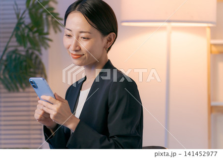 夜、スマホを見るスーツの女性 141452977