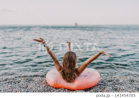 Girl, beach, vacation. Relaxed girl on inflatable donut embracing freedom on a pebble beach with copy space. 141454785