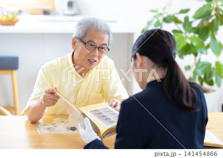 出張買取　自宅で切手や古銭の鑑定をしてもらっているシニア男性　 141454866
