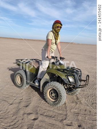 Adventurous woman casual summer outfit confidently rides green quad bike across golden desert dunes, arms raised in celebration, under a bright blue sky dynamic freedom, thrill outdoor exploration. Adventurous woman casual summer outfit confidently rides green quad bike across golden desert dunes, arms raised in celebration, under a bright blue sky dynamic freedom, thrill outdoor exploration. 141455402