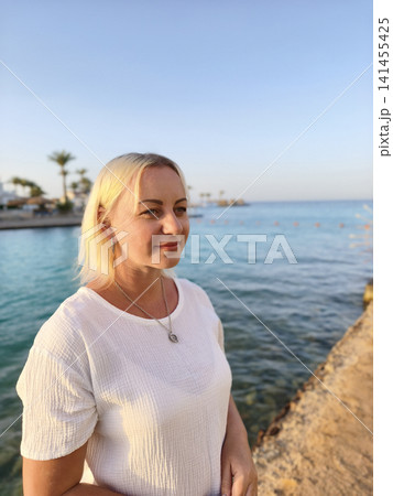 Serene coastal moment a relaxed woman crisp white t shirt smiles gently against backdrop swaying palm trees and tranquil sea, embodying the calm beauty perfect seaside getaway under soft golden sky Serene coastal moment a relaxed woman crisp white t shirt smiles gently against backdrop swaying palm trees and tranquil sea, embodying the calm beauty perfect seaside getaway under soft golden sky 141455425