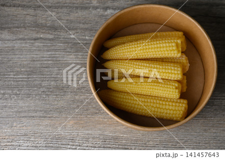 Freshly harvested baby corn in a rustic bowl resting on a weathered wooden table 141457643