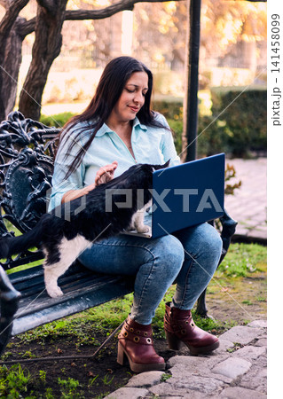Beautiful Latina adult executive woman working in the yard of her house, with her laptop, being teased and interrupted by her cat, with a lot of humor and joy. teleworking, marketing. Beautiful Latina adult executive woman working in the yard of her house, with her laptop, being teased and interrupted by her cat, with a lot of humor and joy. teleworking, marketing. 141458099