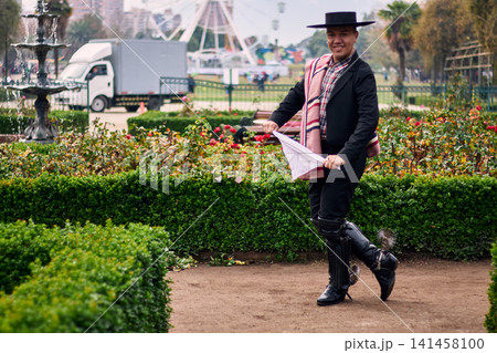 Portrait of a smiling, cheerful young man dressed as a Chilean huaso, celebrating and posing to dance cueca, a traditional Chilean dance. Chilean traditions, celebration, and culture. Portrait of a smiling, cheerful young man dressed as a Chilean huaso, celebrating and posing to dance cueca, a traditional Chilean dance. Chilean traditions, celebration, and culture. 141458100