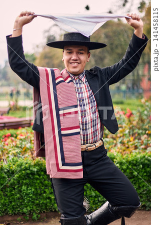 Portrait of a smiling, cheerful young man dressed as a Chilean huaso, celebrating and posing to dance cueca, a traditional Chilean dance. Chilean traditions, celebration, and culture. Portrait of a smiling, cheerful young man dressed as a Chilean huaso, celebrating and posing to dance cueca, a traditional Chilean dance. Chilean traditions, celebration, and culture. 141458115