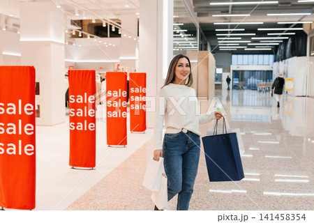 Stylish Woman Carries Shopping Bags in Bright Modern Mall Stylish Woman Carries Shopping Bags in Bright Modern Mall 141458354
