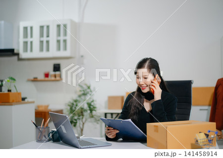 Asian e-commerce entrepreneur live streaming with laptop and parcel boxes. Online seller, content creator, social media marketing, remote business Asian e-commerce entrepreneur live streaming with laptop and parcel boxes. Online seller, content creator, social media marketing, remote business 141458914