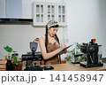 Focused Asian female barista taking stock and managing inventory with a clipboard at a modern cafe counter. 141458947