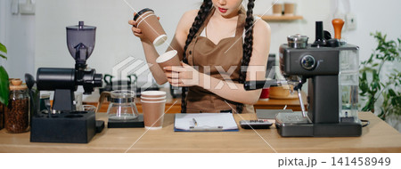 Focused Asian female barista taking stock and managing inventory with a clipboard at a modern cafe counter. Focused Asian female barista taking stock and managing inventory with a clipboard at a modern cafe counter. 141458949