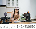 Focused Asian female barista taking stock and managing inventory with a clipboard at a modern cafe counter. 141458950