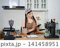 Focused Asian female barista taking stock and managing inventory with a clipboard at a modern cafe counter. 141458951