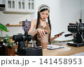 Young Asian female barista preparing fresh roasted coffee beans in a modern cafe kitchen with professional espresso equipment. 141458953