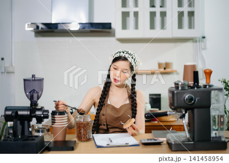 Young Asian female barista preparing fresh roasted coffee beans in a modern cafe kitchen with professional espresso equipment. Young Asian female barista preparing fresh roasted coffee beans in a modern cafe kitchen with professional espresso equipment. 141458954