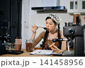 Young Asian female barista preparing fresh roasted coffee beans in a modern cafe kitchen with professional espresso equipment. 141458956