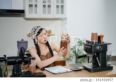 Young Asian female barista preparing fresh roasted coffee beans in a modern cafe kitchen with professional espresso equipment. Young Asian female barista preparing fresh roasted coffee beans in a modern cafe kitchen with professional espresso equipment. 141458957