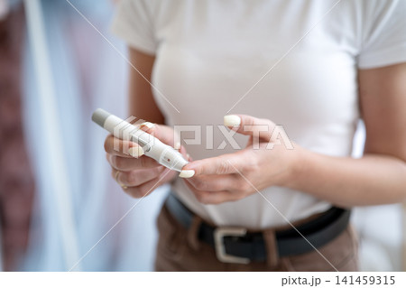Woman using a glucometer to check blood sugar level at home close-up, concept of diabetes control and self-monitoring. Woman using a glucometer to check blood sugar level at home close-up, concept of diabetes control and self-monitoring. 141459315