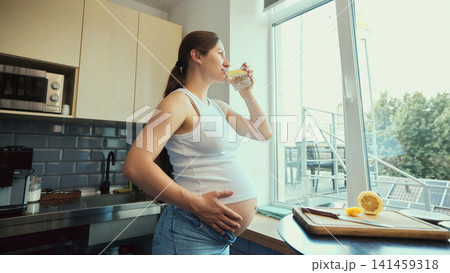 Thirsty young brunette expectant mother drinking water in bright kitchen 141459318