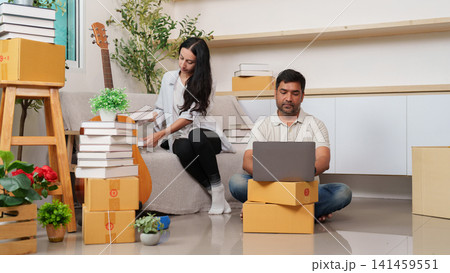 South Asian man working on laptop while couple packs boxes for relocation South Asian man working on laptop while couple packs boxes for relocation 141459551