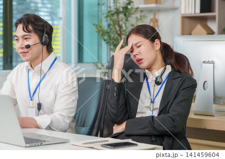 Stressed Asian businesswoman suffering from headache at office desk with colleague 141459604
