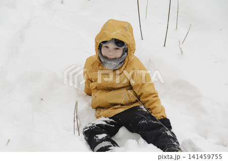 A child in a yellow jacket and gray hat plays in a winter park. A snowy winter forest, a fairy tale. An active, healthy lifestyle and fun games in the snow during the holidays 141459755