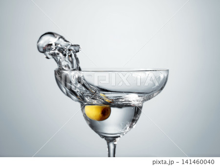 Clear martini glass with green olive in motion. Clear martini glass with green olive in motion. 141460040