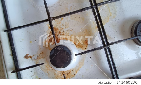 Close up of a dirty white gas stovetop with heavy brown and orange grease stains around a single burner and metal grate... Close up of a dirty white gas stovetop with heavy brown and orange grease stains around a single burner and metal grate... 141460230