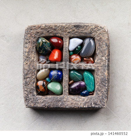 Colorful Tumbled Gemstones in Rustic Stone Tray on Light Surface 141460552