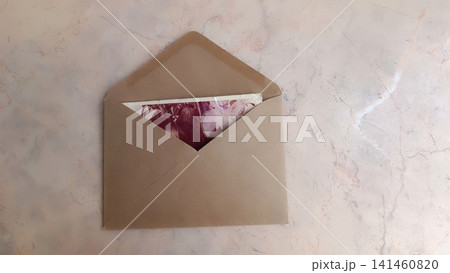 Brown envelope open on pink-grey marble surface, revealing a photo 141460820