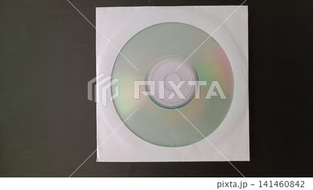 CD inside a white paper sleeve viewed from above, rainbow sheen on the disc visible through the sleeve opening against a dark background. CD inside a white paper sleeve viewed from above, rainbow sheen on the disc visible through the sleeve opening against a dark background. 141460842