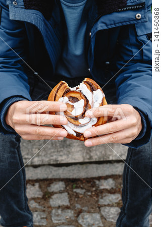 a man holding a bitten danish kanelsnegl on steps a man holding a bitten danish kanelsnegl on steps 141460868