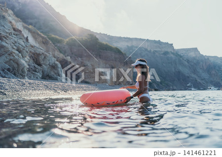 Woman, water, summer vacation at the beach with a pink swimming ring and rocky cliffs. 141461221