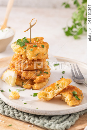 A stack of golden cod fritters on a textured plate with fresh parsley, lemon, and a fork, offering a savory Mediterranean-style seafood appetizer snack A stack of golden cod fritters on a textured plate with fresh parsley, lemon, and a fork, offering a savory Mediterranean-style seafood appetizer snack 141461367