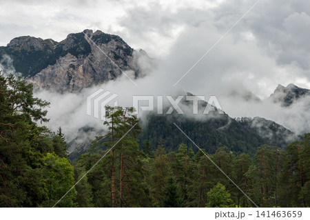 Rugged Dolomite crags wrapped in clouds above conifer forest, near San Vigilio di Marebbe 141463659