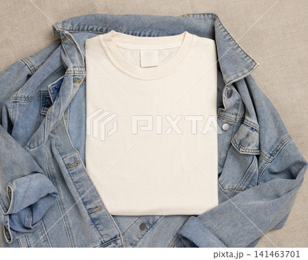 Blank light beige folded shirt mockup over blue denim jacket, crewneck template for print on demand Blank light beige folded shirt mockup over blue denim jacket, crewneck template for print on demand 141463701